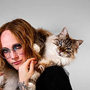 Calypso a rejoint le concours — aidez-le/la à gagner de superbes lots ! person, cat, glasses, tattoo, red_hair, blue_eyeshadow, fluffy_cat, blue_eyes, face, hand, shoulder, portrait, indoor, light_background, nose_ring, casual_clothing, pet, animal, closeup, friendly