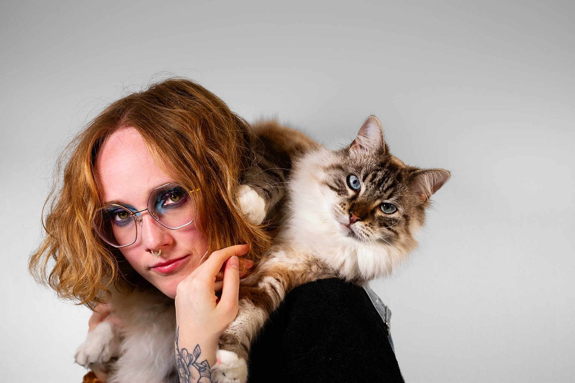Calypso a rejoint le concours — aidez-le/la à gagner de superbes lots ! person, cat, glasses, tattoo, red_hair, blue_eyeshadow, fluffy_cat, blue_eyes, face, hand, shoulder, portrait, indoor, light_background, nose_ring, casual_clothing, pet, animal, closeup, friendly