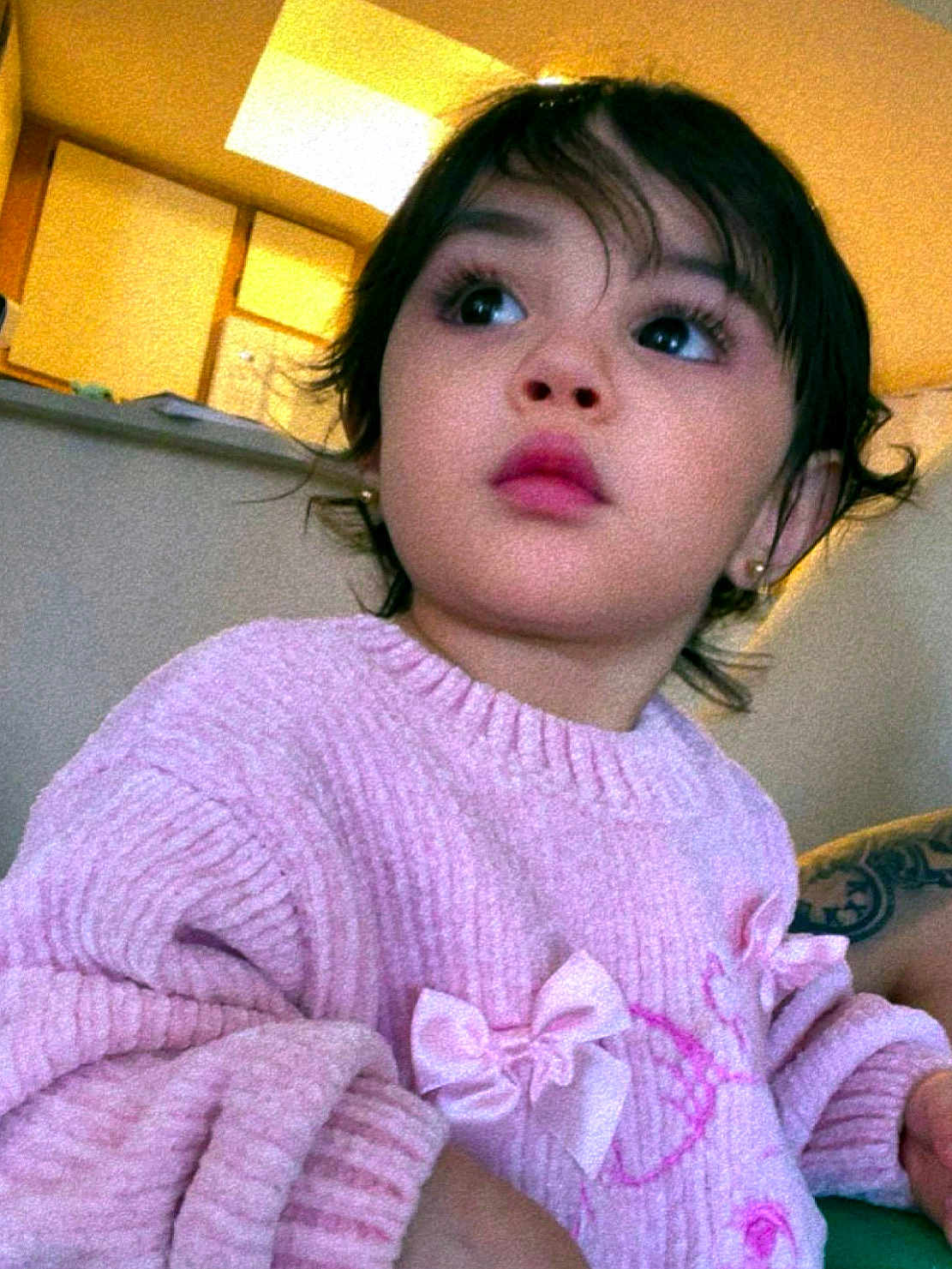 Zeynep is registered to the contest to win money with this photo: child, toddler, pink_sweater, bow, indoor, portrait, face, curly_hair, long_eyelashes, rosy_lips, warm_lighting, cozy, expression, person, cute, young_child, casual_clothing, soft_texture, looking_away, home