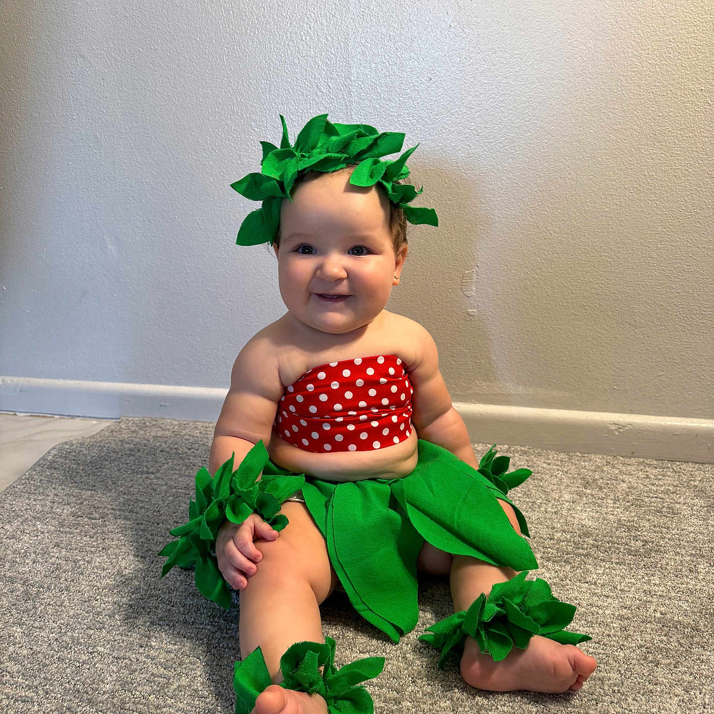 Micaela joined the competition — help win amazing prizes! adorable, ankle_bands, baby, barefoot, carpet, child, costume, cute, green_leaves, happy, headwear, indoor, leaf_accessories, plush, portrait, red_polka_dot, sitting, smiling, wall, wristbands
