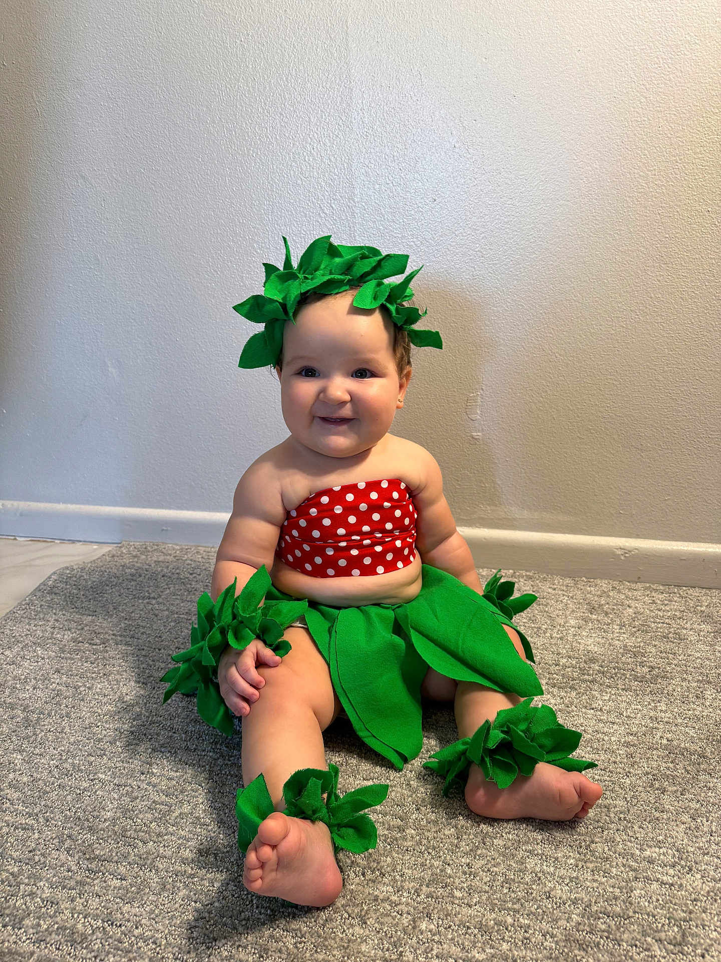 Micaela joined the competition — help win amazing prizes! baby, child, smiling, costume, leaf_accessories, red_polka_dot, green_leaves, carpet, indoor, cute, sitting, barefoot, wall, adorable, headwear, wristbands, ankle_bands, plush, portrait, happy