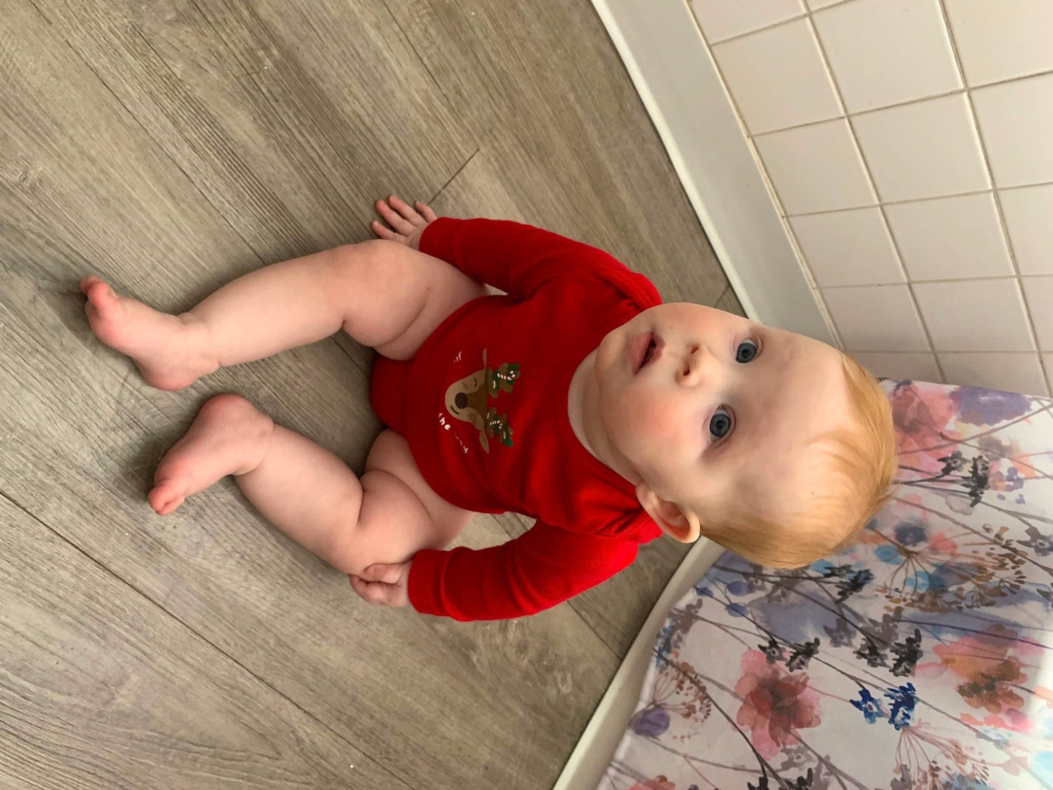 Luna is registered to the contest to win money with this photo: baby, baby_toddler_clothing, carmine, child, comfort, face, floor, flooring, foot, fun, hardwood, human_body, human_leg, knee, pattern, person, sock, surprise, thigh, toddler