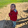 bench, casual_clothing, child, coat, grass, looking_up, outdoors, park, people, picnic_table, playground, red_jacket, sand, shadow, sneakers, standing, stroller, sunlight, toddler, trees