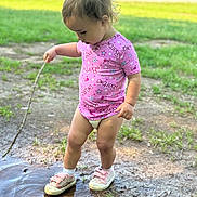 Arizona is registered to the contest to win money with this photo: toddler, child, outdoor, puddle, stick, grass, pink_shirt, barbie, shoes, socks, play, mud, nature, exploration, summer, young_child, concentration, casual_clothing, bare_legs, sunlight