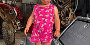 Arizona is registered to the contest to win money with this photo: butterfly_pattern, child, concrete_floor, cooler, curious_expression, garage, helmet, ice, indoor, motorbike, person, pink_clothing, shorts, sleeveless_shirt, standing, storage, toddler, tools, toy_pool, workshop