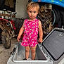 Arizona is registered to the contest to win money with this photo: toddler, child, pink_clothing, butterfly_pattern, cooler, ice, garage, motorbike, tools, helmet, concrete_floor, curious_expression, shorts, sleeveless_shirt, toy_pool, storage, workshop, person, standing, indoor