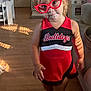 barefoot, bulldogs, casual, cheerleading_outfit, child, clothing, couch, curious_expression, furniture, glasses, home, indoor, natural_light, person, portrait, red_glasses, smile, toddler, wooden_floor, young_child