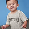 child, toddler, smiling, happy, portrait, boy, short_hair, grey_tshirt, new_york, indoor, blue_background, cute, casual_clothing, young_child, person, face, standing, expression, joyful, playful