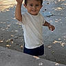 child, boy, smiling, waving, outdoor, daylight, shade, concrete, sculpture, playground, casual_clothing, white_shirt, shorts, happy, portrait, person, young, curly_hair, park, nature