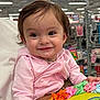 baby, child, pink_hoodie, smile, face, person, indoor, store, shopping, colorful_ribbons, hand, sleeve, clothing, toy, aisle, shelf, retail, happy, cute, holding