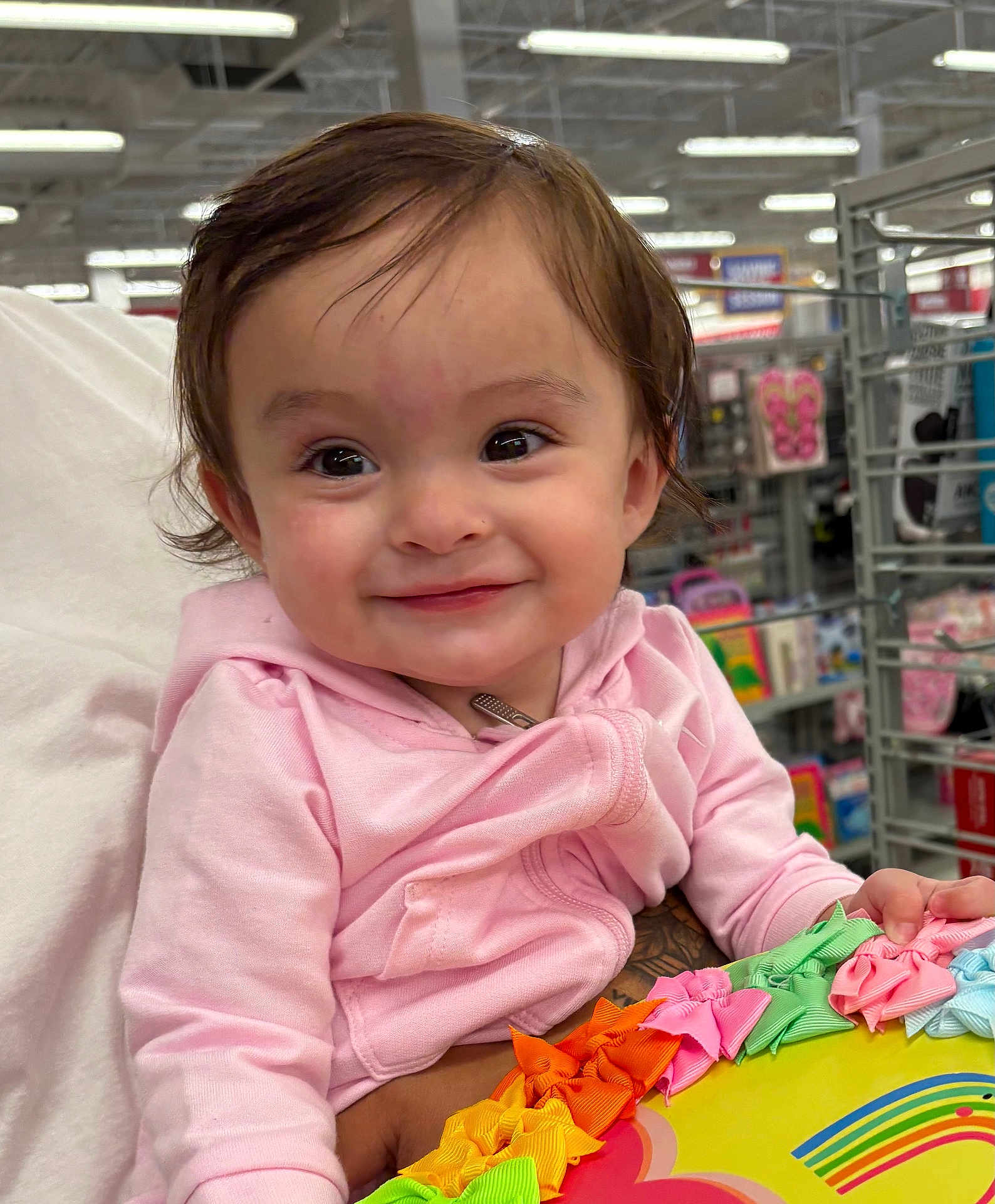 Galilea is registered to the contest to win money with this photo: baby, child, pink_hoodie, smile, face, person, indoor, store, shopping, colorful_ribbons, hand, sleeve, clothing, toy, aisle, shelf, retail, happy, cute, holding