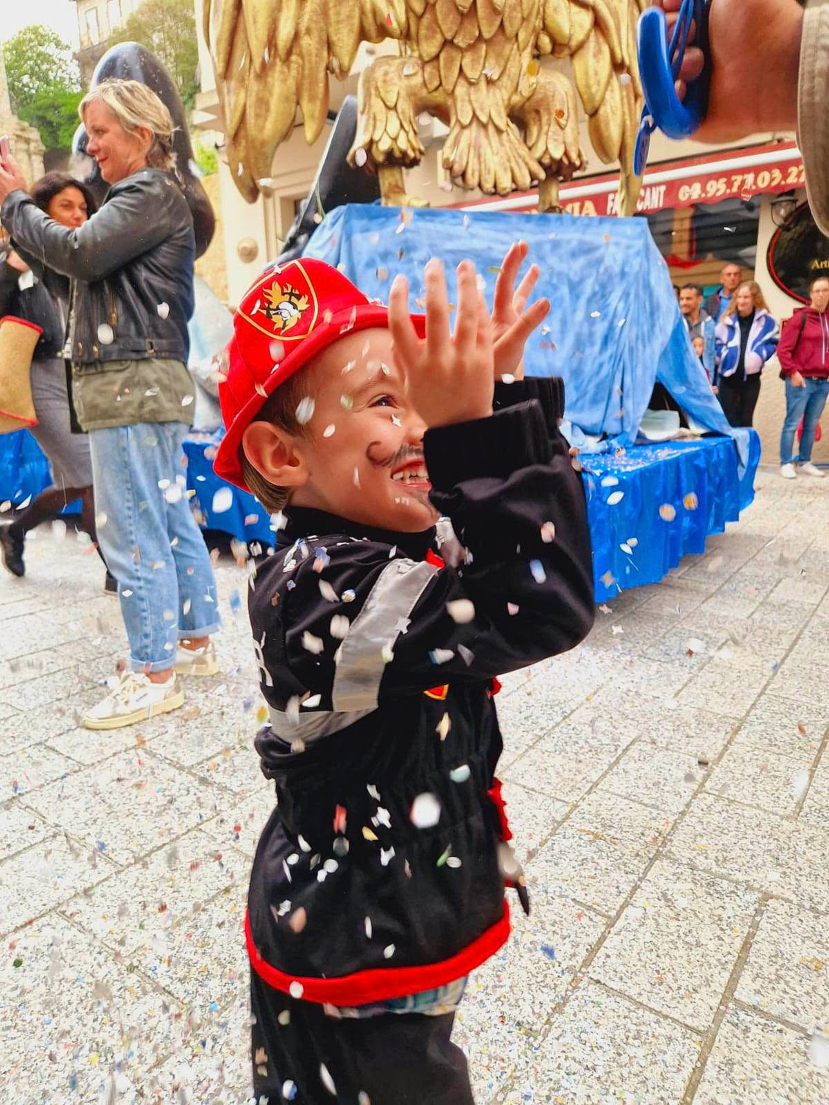 Enzo a rejoint le concours — aidez-le/la à gagner de superbes lots ! backpack, bag, blurred, child, costume, crowd, event, fun, happy, headwear, joy, leisure, luggage_and_bags, pedestrian, person, public_event, road, street, t_shirt, toddler