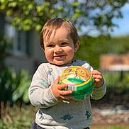 Eden a rejoint le concours — aidez-le/la à gagner de superbes lots ! toddler, child, ball, outdoor, sunlight, smile, happy, sweater, dinosaur_pattern, grass, garden, background_blur, playful, person, portrait, nature, daylight, cute, young_child, holding_object