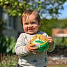 toddler, child, ball, outdoor, sunlight, smile, happy, sweater, dinosaur_pattern, grass, garden, background_blur, playful, person, portrait, nature, daylight, cute, young_child, holding_object