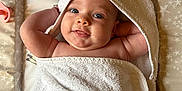 Annabelle is registered to the contest to win money with this photo: baby, towel, infant, smile, face, skin, hand, blanket, hooded_towel, changing_mat, star_pattern, cute, lying_down, child, newborn, happy, indoors, person, soft_texture, playful