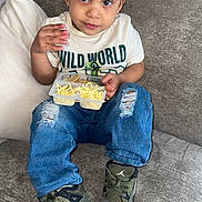 Kaius joined the competition — help win amazing prizes! casual_clothing, child, couch, curly_hair, cute, food_container, green_shoes, indoor, jeans, living_room, looking_up, pillows, relaxed, ripped_jeans, shirt, sitting, snack, sneakers, toddler, wild_world_shirt