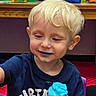 birthday, blonde_hair, blue_frosting, cake, celebration, child, clothing, cupcake, face, food, gift_bags, happy, indoor, party, person, sitting, smiling, table, toddler, young_child
