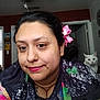 woman, cat, indoor, smile, flower, hair_accessory, face, portrait, white_cat, casual_clothing, home, door, ceiling_fan, wall_art, necklace, colorful_clothing, relaxed, pet, curious, background