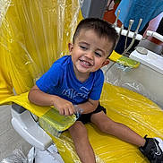 Isaiah Rivera is registered to the contest to win money with this photo: child, boy, smiling, dental_chair, yellow_chair, plastic_cover, blue_shirt, black_shoes, short_hair, indoor, dentist_office, floor, person, happy, sitting, medical_equipment, waiting, casual_clothing, shoe, healthcare