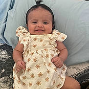 Jazlyn is registered to the contest to win money with this photo: baby, child, smiling, dress, flower_pattern, bed, pillow, cute, happy, indoors, person, infant, hair_tie, pattern, fabric, skin, face, small_hands, lying_down, comfort