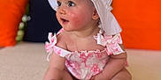 Bonnie joined the competition — help win amazing prizes! baby, child, hat, white_hat, pink_outfit, sitting, curious, indoor, cushions, orange_cushion, green_foliage, closeup, portrait, soft_lighting, cute, infant, small_hand, small_feet, expression, skin