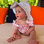 baby, child, hat, white_hat, pink_outfit, sitting, curious, indoor, cushions, orange_cushion, green_foliage, closeup, portrait, soft_lighting, cute, infant, small_hand, small_feet, expression, skin
