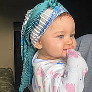 Jena participe au concours pour gagner de l'argent avec cette photo : baby, child, face, blue_eyes, headscarf, floral_clothing, onesie, indoor, portrait, cute, nibbling, hand, person, soft_lighting, holding, patterned_fabric, smile, toddler, closeup, cozy