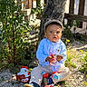 beige_pants, blue_shirt, boy, cap, child, cute, daylight, garden, gravel, kinder, nature, outdoor, plants, playful, sitting, sunlight, toddler, toy, tree, young_child