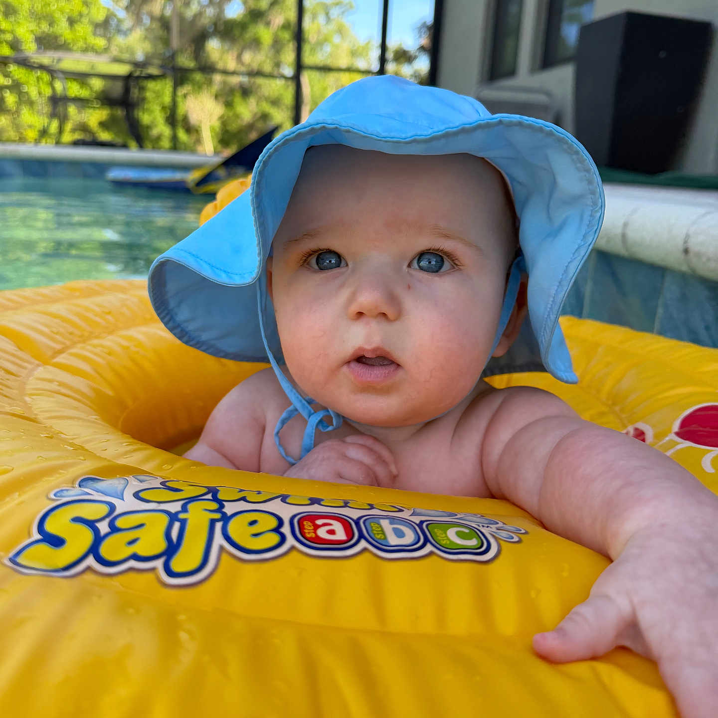 Grayson joined the competition — help win amazing prizes! baby, infant, blue_hat, yellow_inflatable, pool, water, outdoor, summer, child, face, skin, arm, expression, sunlight, swimming, recreation, closeup, daytime, nature, house