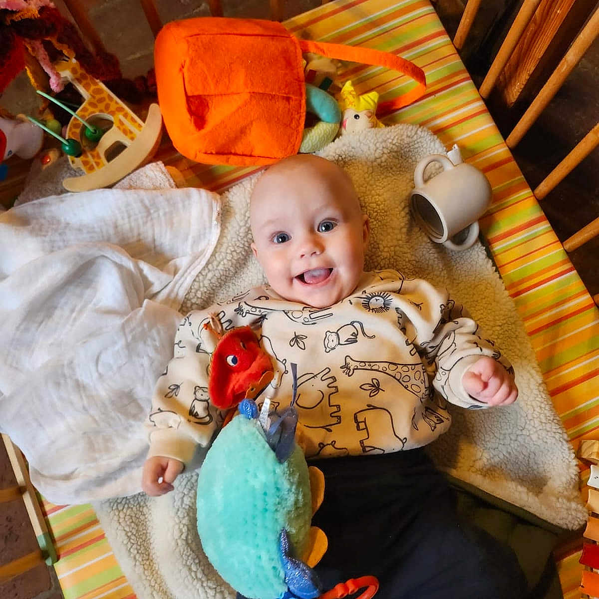 Timothé a rejoint le concours — aidez-le/la à gagner de superbes lots ! animal_print, baby, blanket, child, colorful, cozy, crib, cushion, cute, happy, indoor, infant, mug, playful, plush_toy, smiling, striped, sweater, toy, wooden