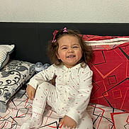 Madlen Lazarova a rejoint le concours — aidez-le/la à gagner de superbes lots ! toddler, child, smiling, pajamas, hair_clips, bed, pillow, baby_bottle, indoor, patterned_bedspread, white_clothing, happy, cute, sitting, person, cozy, home, young_child, playful, casual