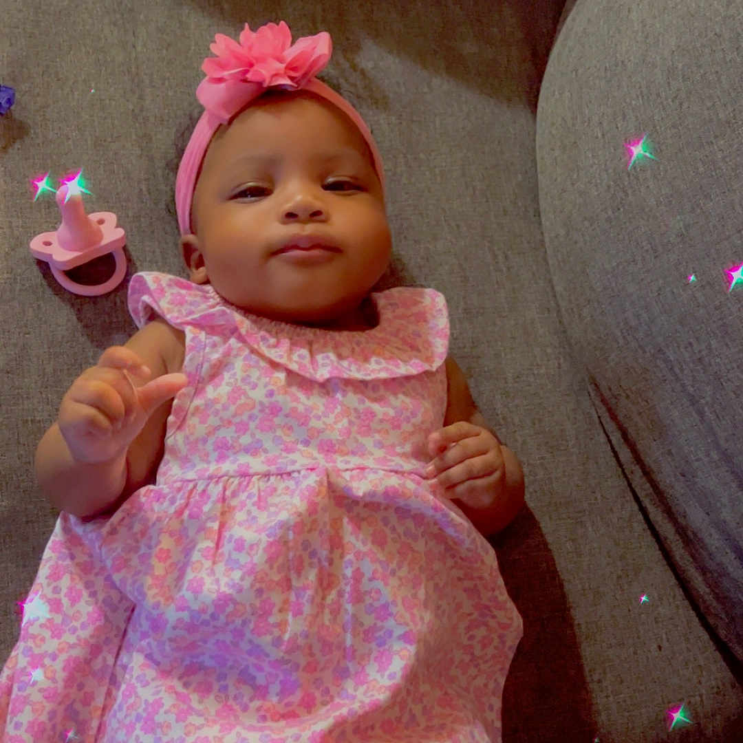 Kehlani joined the competition — help win amazing prizes! baby, child, infant, portrait, smiling, sitting, lying_down, pink_dress, floral_pattern, flower_headband, pacifier, couch, indoor, home, fashion, sparkles, digital_effect, happy, face, photography