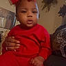 baby, infant, child, portrait, red_outfit, bow, hair_bow, sitting, indoor, couch, adult_hand, face, serious_expression, sparkles, digital_effect, home, furniture, closeup, fashion, family