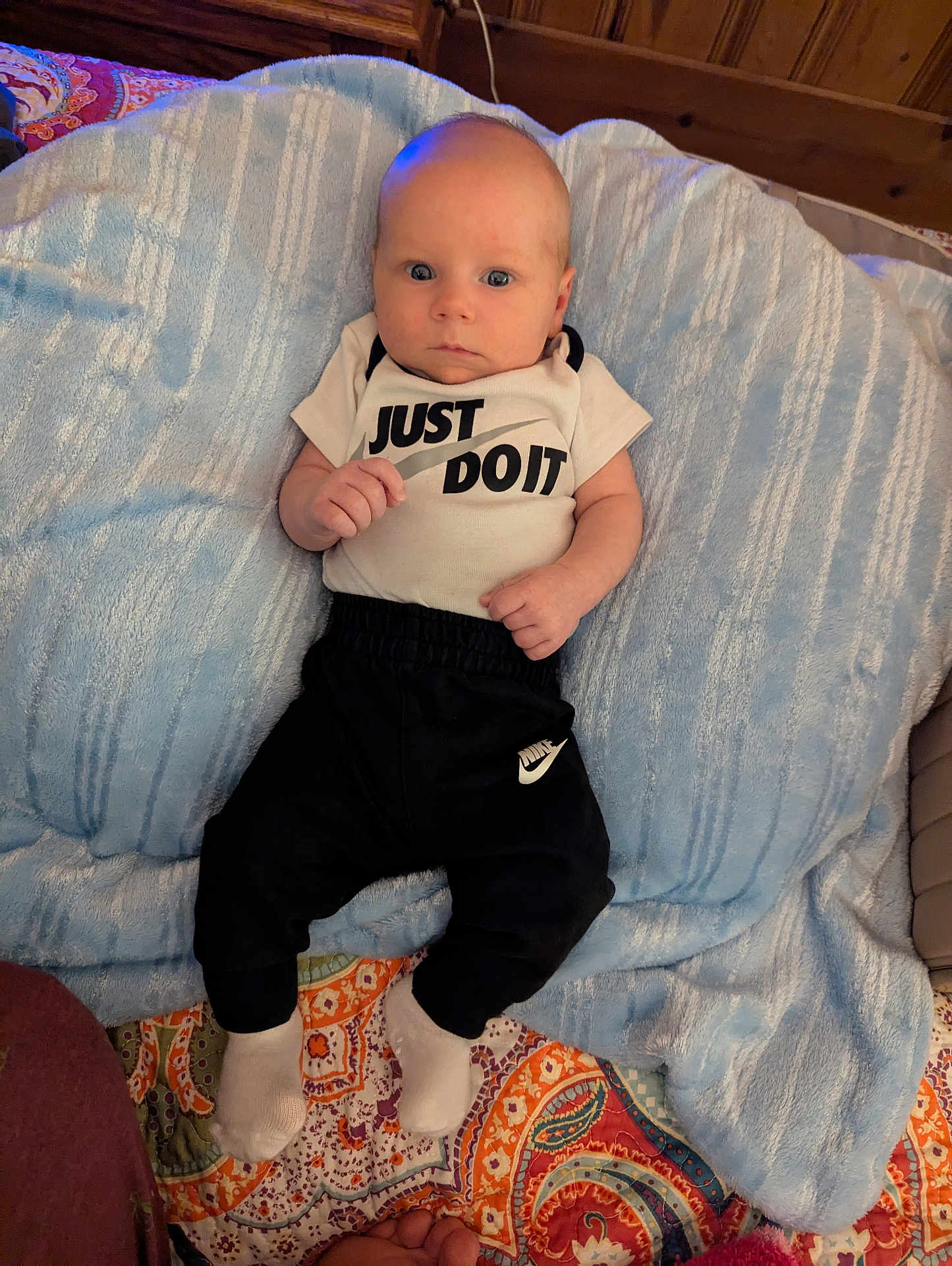 Oaklee joined the competition — help win amazing prizes! baby, infant, blanket, clothing, pants, socks, face, person, indoor, bed, patterned_quilt, wooden_wall, blue_blanket, nike, onesie, footwear, cute, young_child, portrait, lying_down