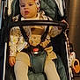 baby, stroller, child, headband, clothing, shoes, safety_harness, face, person, indoor, curious, seated, cute, toddler, fashion, footwear, toy, hand, fabric, comfort