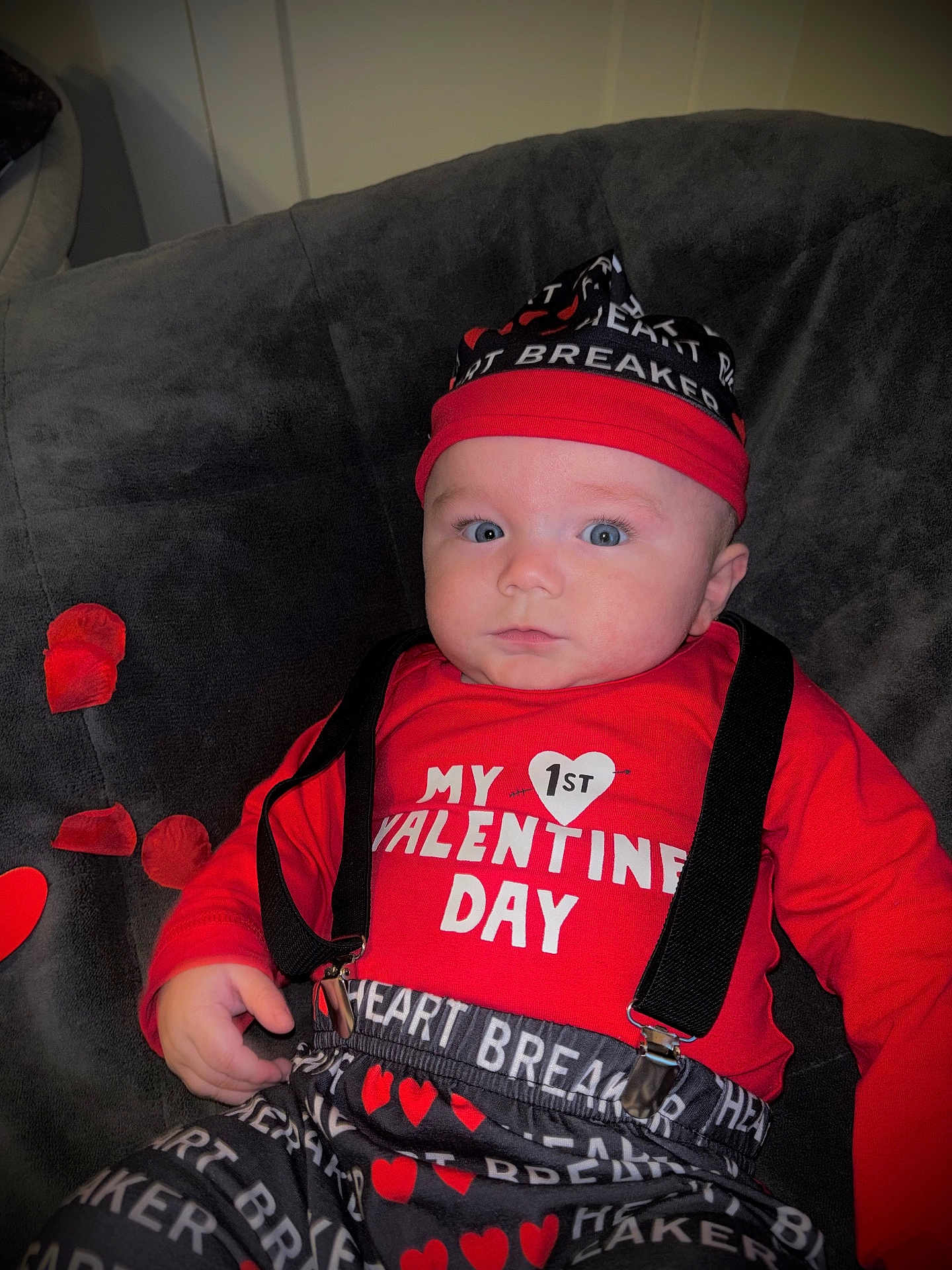 Zylis is registered to the contest to win money with this photo: baby, infant, child, valentines_day, red_clothing, hat, suspenders, heart_pattern, couch, rose_petals, portrait, close_up, blue_eyes, indoor, cute, expression, holiday_outfit, lying_down, soft_fabric, photography