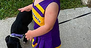Charlotte is registered to the contest to win money with this photo: toddler, child, pacifier, puppy, dog, leash, sidewalk, grass, brick_wall, purple_dress, yellow_trim, outdoor, curious, cute, small_dog, person, footwear, sock, pet, summer