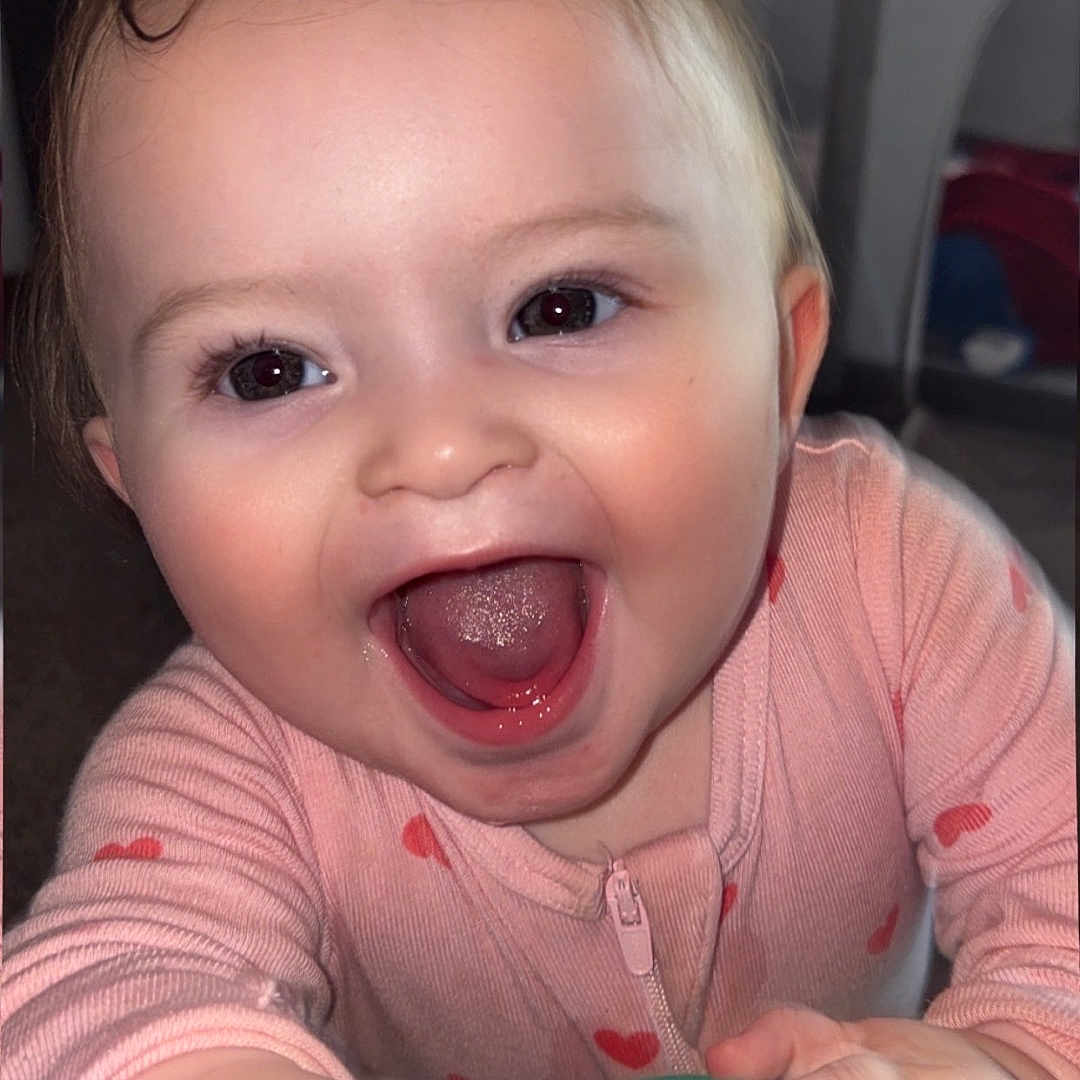 Asmira joined the competition — help win amazing prizes! baby, child, smiling, happy, face, hand, pink_clothing, heart_pattern, indoor, closeup, cute, infant, young_child, person, portrait, expression, joy, playful, warm_lighting, candid