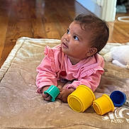 Naomi a rejoint le concours — aidez-le/la à gagner de superbes lots ! baby, infant, child, pink_clothing, blanket, toy, stacking_cups, floor, wood_floor, indoor, curious, cute, young_child, playing, soft_texture, candid, portrait, toddler, cozy, home