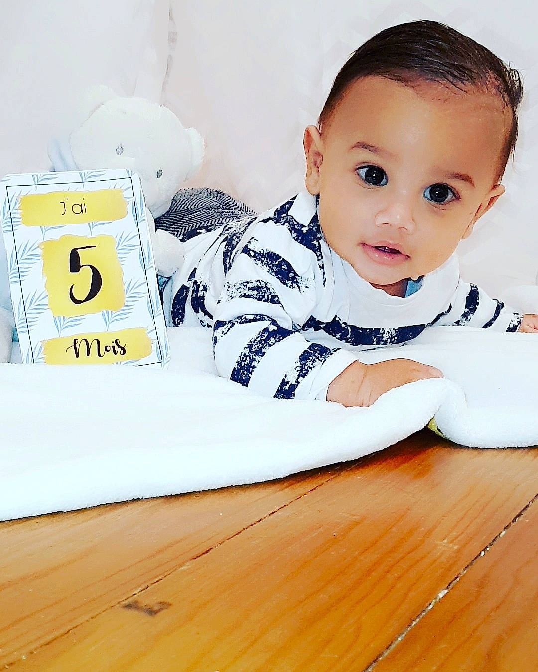 Selyan participe au concours pour gagner de l'argent avec cette photo : baby, baby_toddler_clothing, child, comfort, eyelash, facial_expression, flooring, font, hairstyle, happy, hardwood, mammal, person, sitting, sleeve, t_shirt, table, toddler, varnish, wood