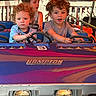 child, children, amusement_ride, car, steering_wheel, curly_hair, short_sleeves, outdoor, daylight, play, fun, kids, face, vehicle, seat, smile, concentration, colorful, hands, young