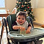 Noa a rejoint le concours — aidez-le/la à gagner de superbes lots ! baby, high_chair, smiling, food_mess, bib, cup, christmas_tree, decorations, indoor, wooden_chair, table, window, floor, happy, child, person, home, holiday, festive, cozy