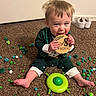 baby, child, carpet, pom_poms, toy, plaque, sitting, smiling, indoor, clothing, barefoot, green, white_shoes, floor, door, happy, cute, infant, playful, portrait