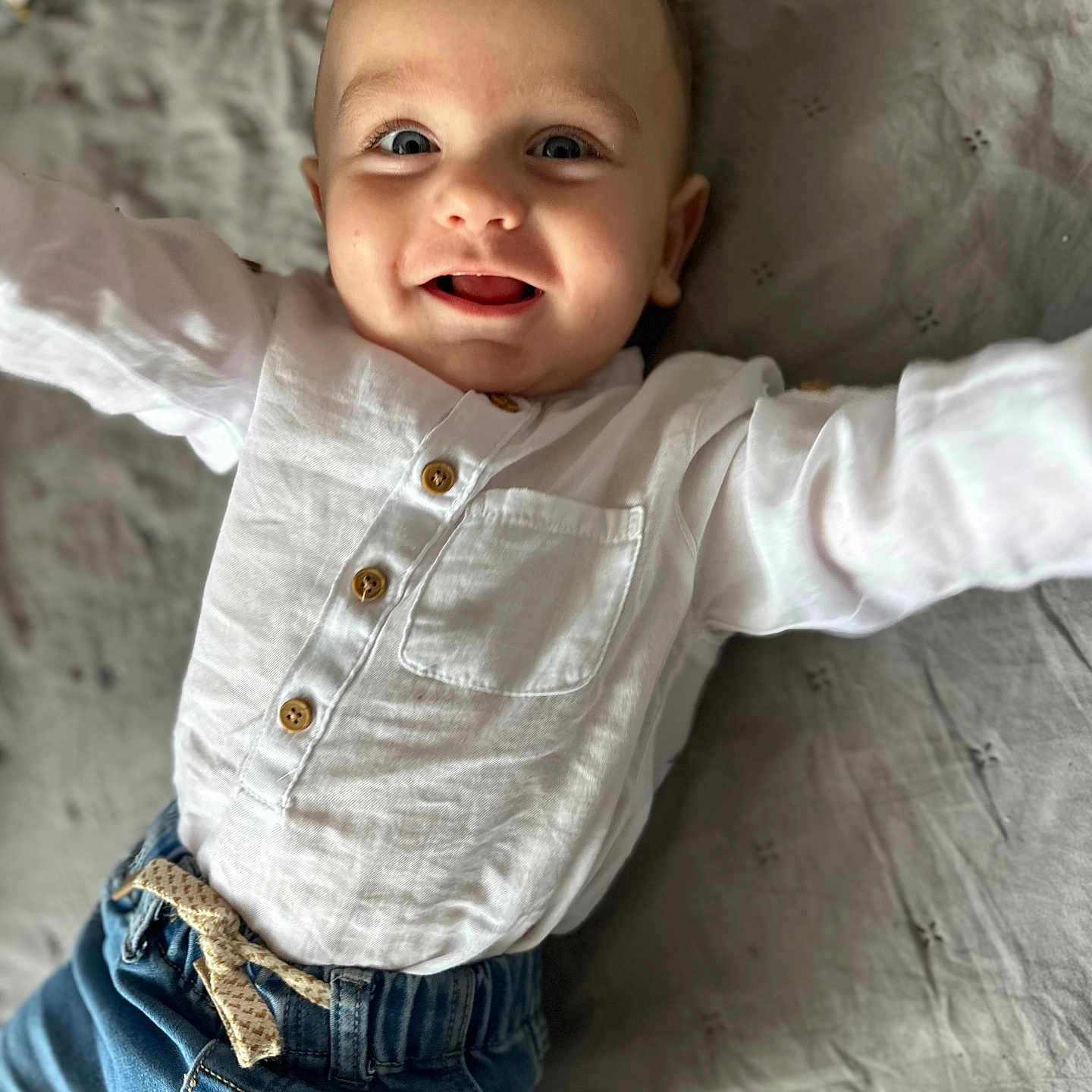 Nikodem is registered to the contest to win money with this photo: arms_outstretched, baby, blanket, blue_jeans, buttoned_shirt, casual_clothing, child, closeup, cute, denim, fabric, face, happy, indoor, infant, lying_down, person, portrait, smiling, white_shirt