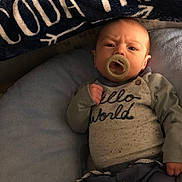 Coda is registered to the contest to win money with this photo: baby, pacifier, infant, clothing, blanket, cushion, face, person, portrait, indoors, cozy, blue, text, hand, newborn, lying_down, cute, expression, button, sleeves