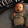baby, pacifier, infant, clothing, blanket, cushion, face, person, portrait, indoors, cozy, blue, text, hand, newborn, lying_down, cute, expression, button, sleeves