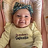 Kinslee is registered to the contest to win money with this photo: baby, infant, smile, headband, clothing, sitting, baby_seat, pink, beige, patterned_fabric, happy, cute, portrait, child, young_child, indoor, person, face, apparel, text_on_clothing