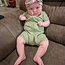 Kinslee is registered to the contest to win money with this photo: baby, infant, child, headband, green_onesie, couch, leather, furniture, indoor, portrait, sitting, cute, chubby, fists, expression, headwear, skin, legs, feet, home