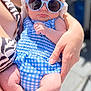 baby, sunglasses, hat, blue_clothing, checkered_pattern, adult_hand, outdoor, sunlight, person, infant, fashion, summer, accessory, skin, arm, holding, serious_expression, closeup, cute, casual
