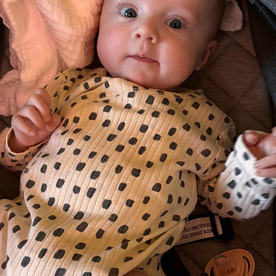 Orla is registered to the contest to win money with this photo: baby, blanket, child, closeup, clothing, cute, expression, face, gaze, hand, human, indoors, infant, lying_down, newborn, pacifier, polka_dot, portrait, skin, soft_toys